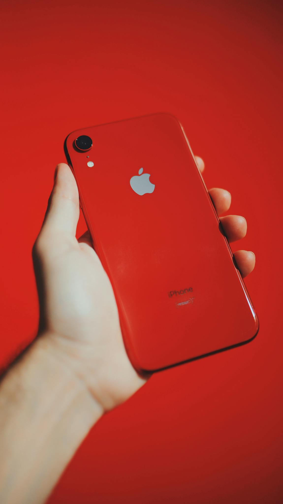 A red smartphone held in a hand against a matching red background, emphasizing modern technology.